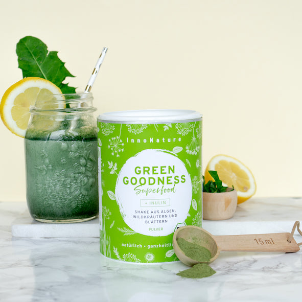 gruene-shakedose-daneben-gefuelltes-glas-mit-gruenem-shake-zitrone-holzloeffel-und-kraeuter-als-deko