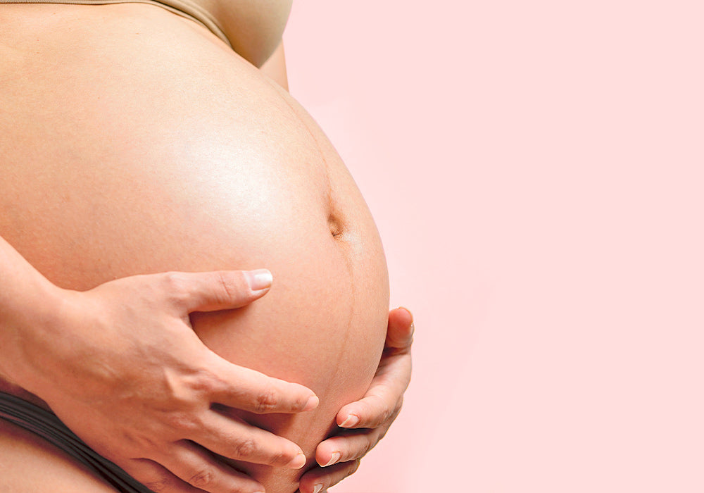 Schwangerer Bauch einer Frau vor rosa Hintergrund