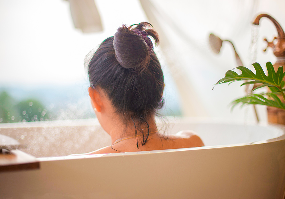 Frau sitzt in Badewanne.