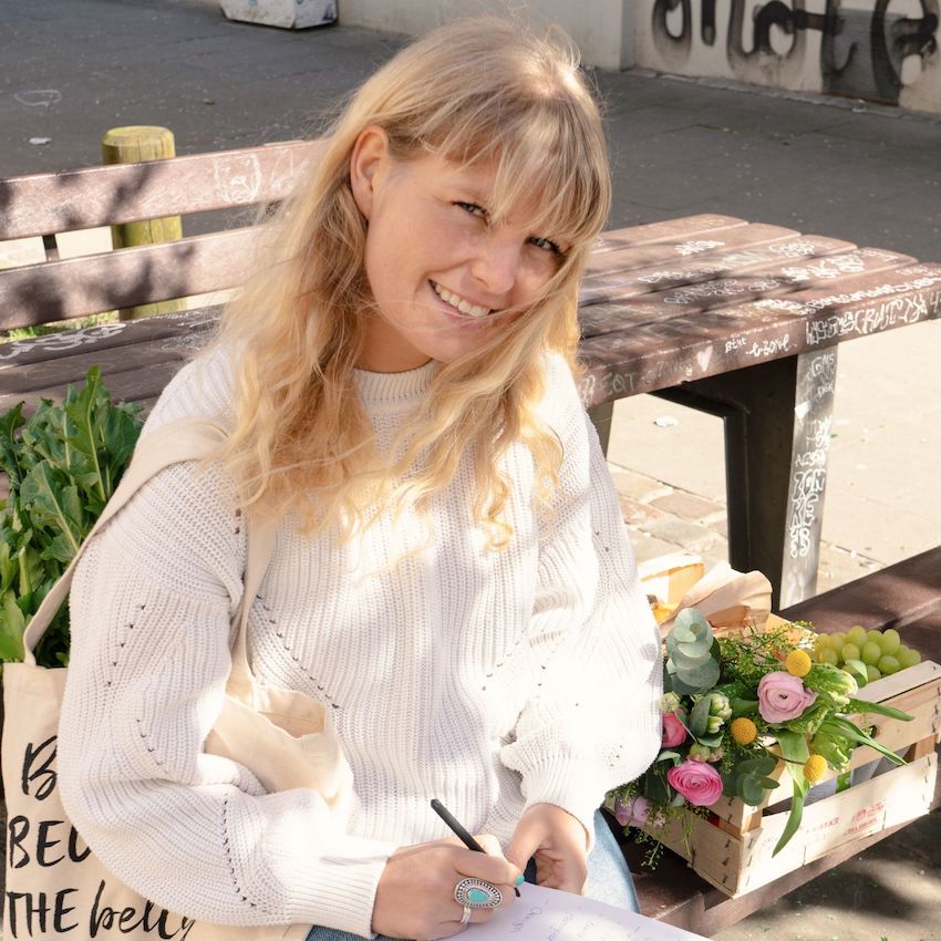 Julia schreibt etwas auf ein Blatt Papier und lächelt in die Kamera