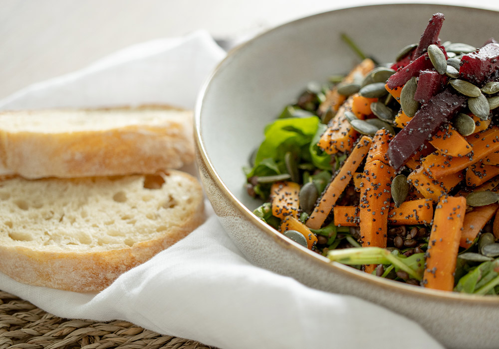 Linsen-Ofengemüse-Salat mit Mohn und Pflaumendressing und Ciabatta Brot auf einer weißen Tischdecke