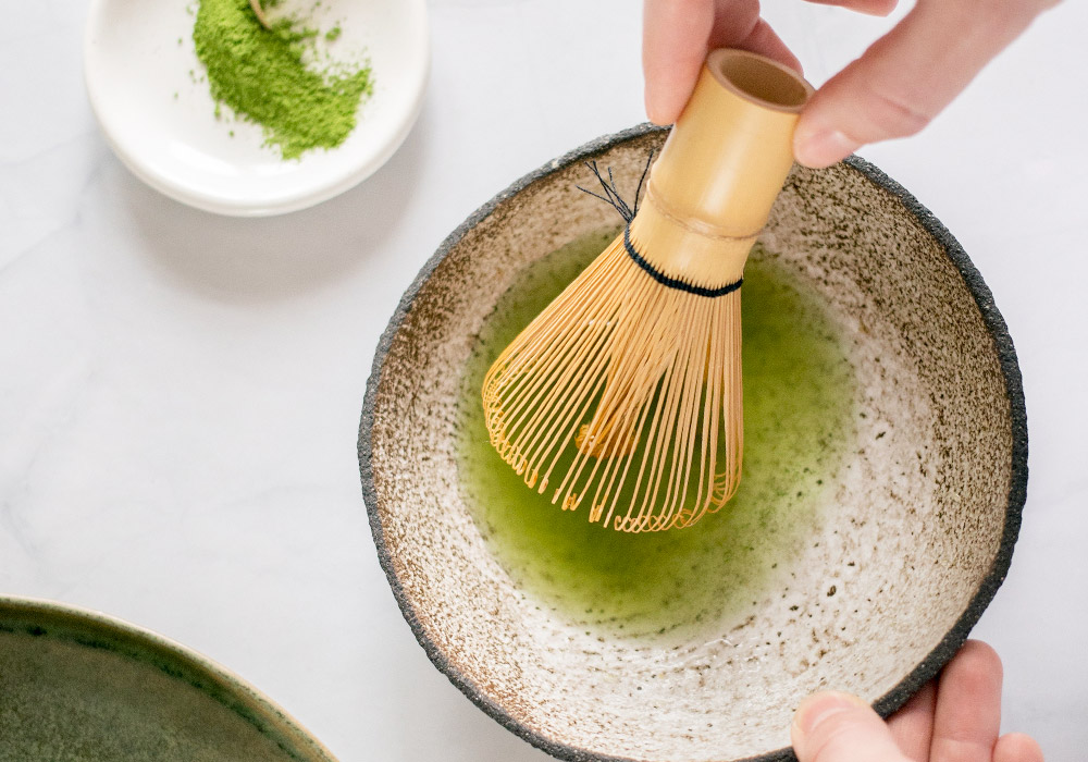 Matcha wird in einer Schale mit einem Bambusbesen angeruehrt.