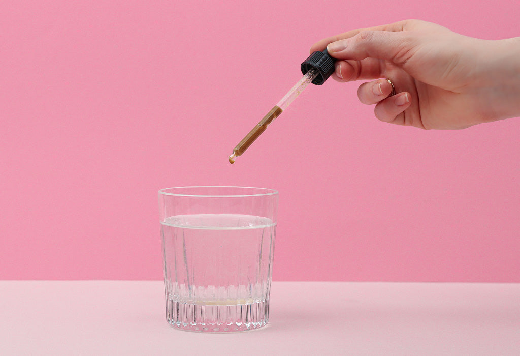 Eine Pipette mit Maca wird in ein Wasserglas getropft.