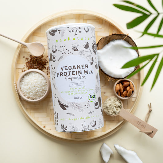 Veganer Protein Mix auf einem geflochtenen Tablett mit Zutaten drapiert