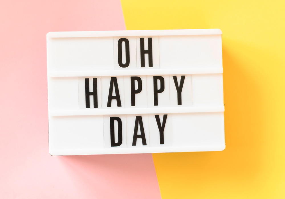 Die Worte "Oh Happy Day" auf weißem Hintergrund vor einem rosa-gelben Hintergrund