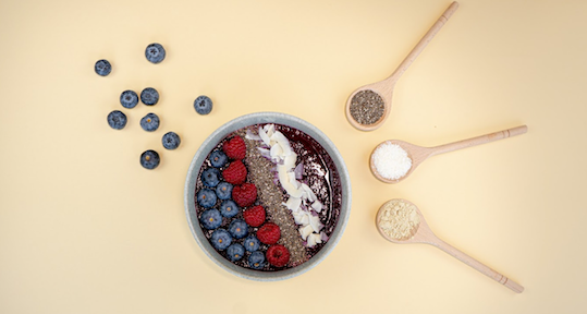schale-mit-beeren-kokosraspeln-chiasamen-daneben-drei-loeffel-mit-unterschiedlichen-pulvern