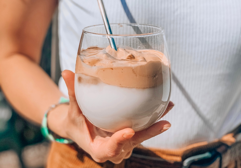 Hand hält Eiskaffee in einem Glas mit Metallstohhalm
