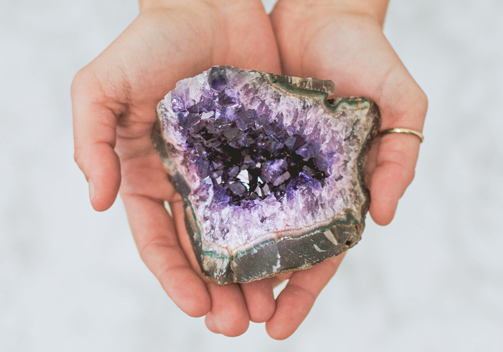 Weibliche Hände, die einen Amethysten halten.