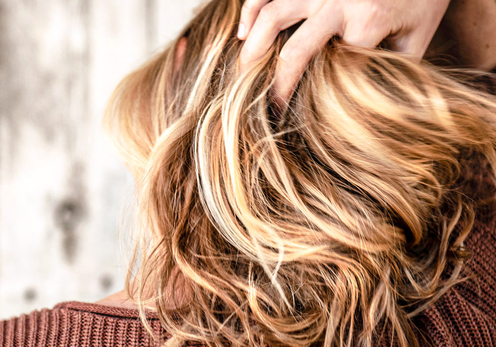 Frau mit blondem Haar fährt sich mit einer Hand durch die Haare.