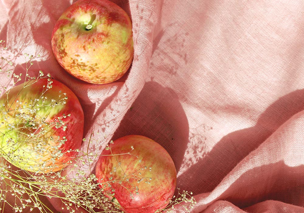 Drei Äpfel liegen auf einer rosa Tischdecke. 