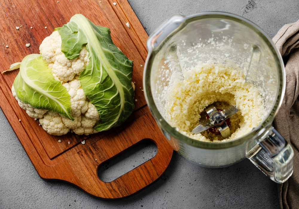 Blumenkohl auf einem Holzbrett und zerkleinert in einem Mixer