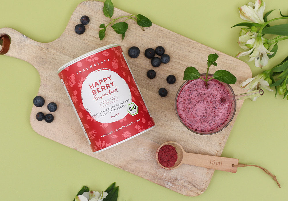 InnoNature Happy Berry Shake auf einem Holztablett, dekoriert mit Blumen und frischen Beeren