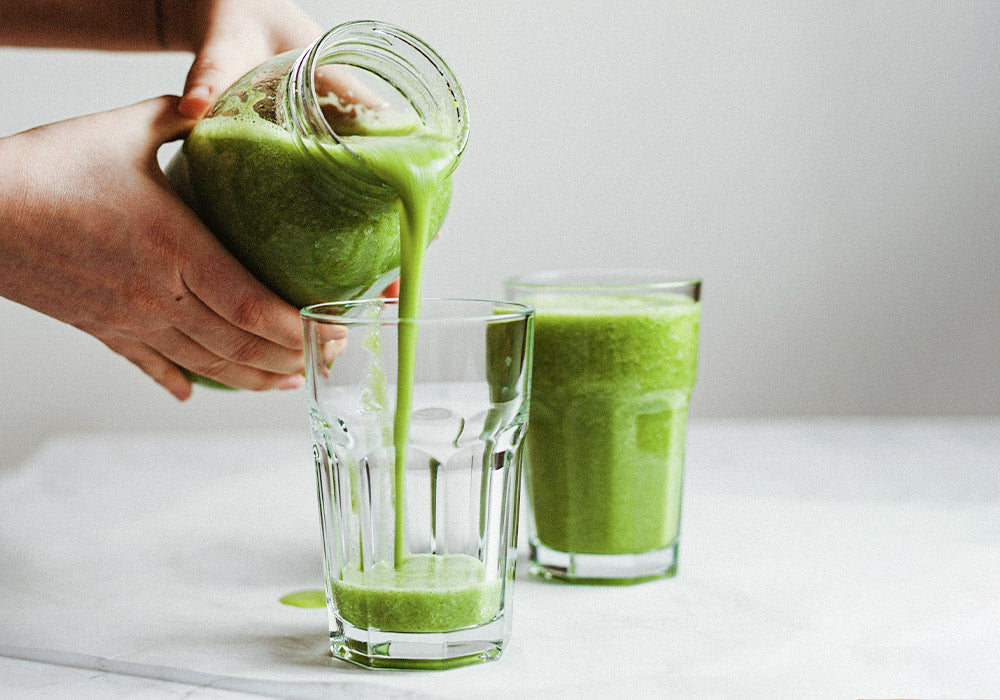 Hand mit grünem Smoothie auf blauem Hintergrund