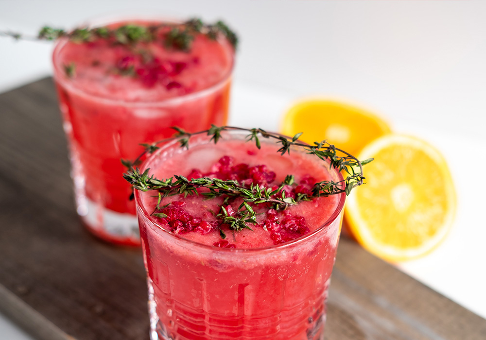 Glas mit durchsichtiger Flüssigkeit, Eiswürfeln, Limettenscheiben und Rosmarinzweig auf einer weißen Tischdecke. Daneben Rosmarin und Limetten als Deko.