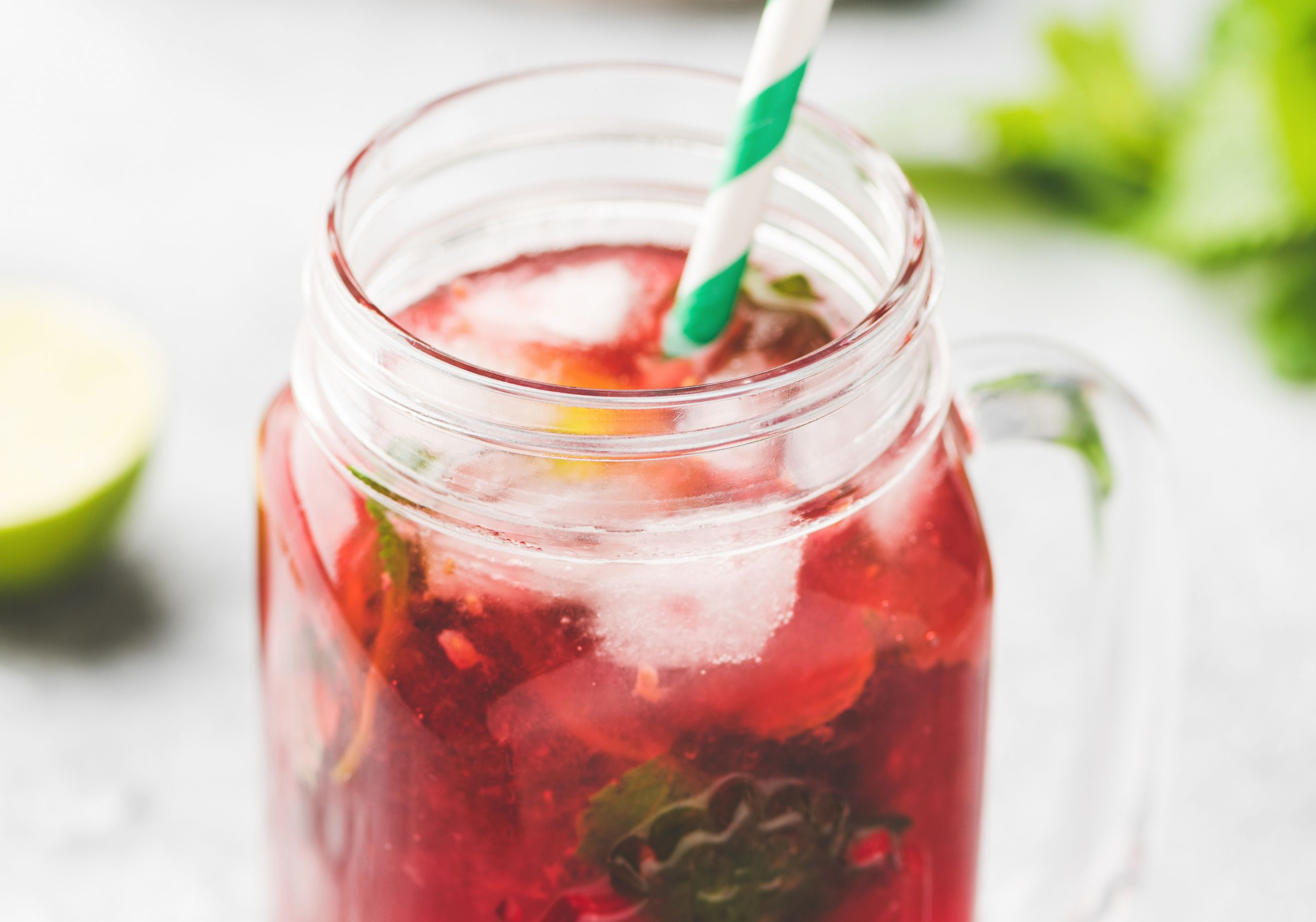 Glas mit rotem Tee und Eiswürfeln. Darin ein grün-weißer Papier-Strohhalm 