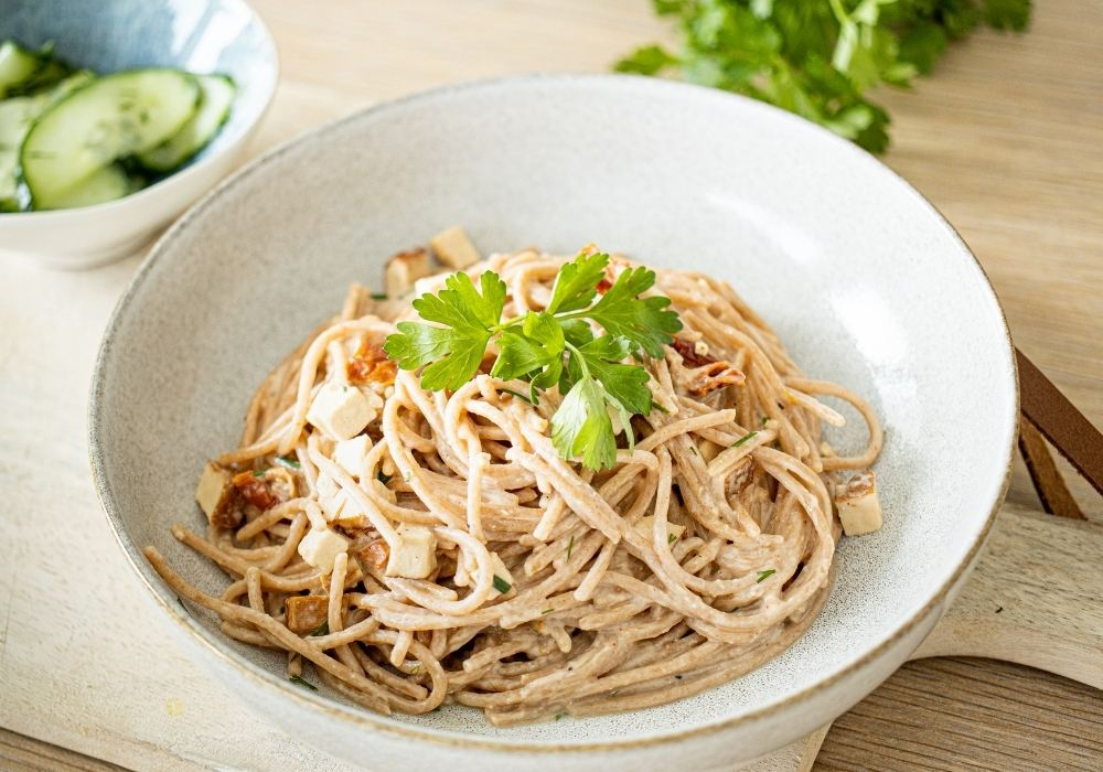 Ein Teller mit veganer Spaghetti Carbonara und Gurkensalat.