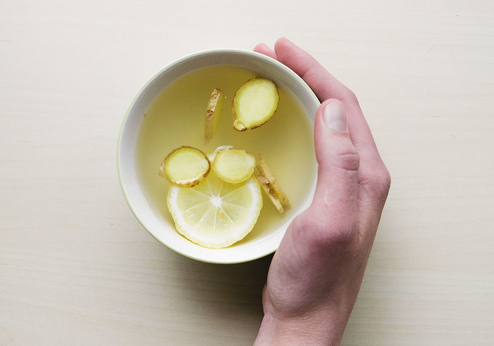 Hand hält Tasse mit heißem Ingwer-Zitrone-Tee umschlossen