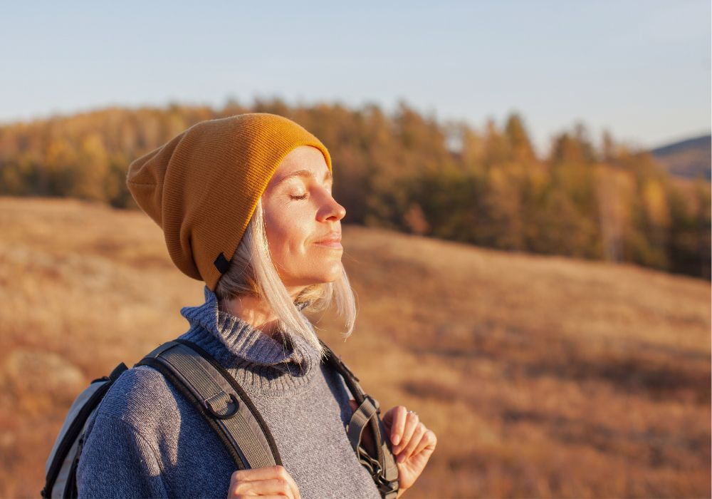 Person mit langen weißblonden Haaren und Mütze genießt Sonne beim Wandern