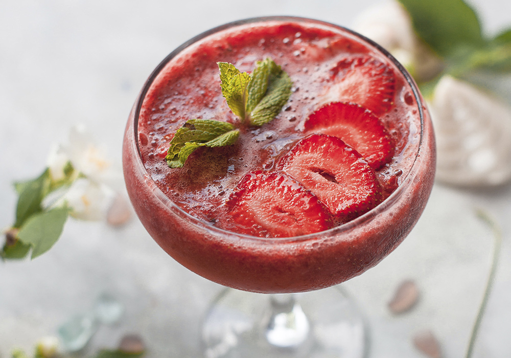 Martiniglas gefüllt mit einem roten smoothie-ähnlichen Getränk und Erdbeeren.