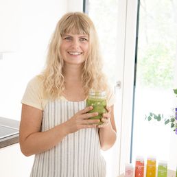 Julia hält einen Smoothie in der Hand und lacht in die Kamera