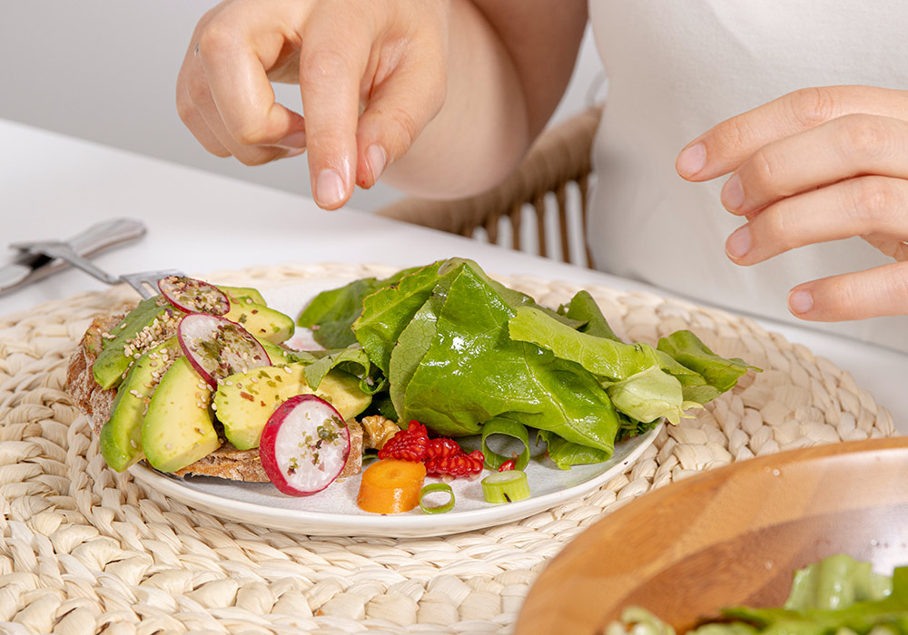 Teller mit Salatblättern, Möhre, Radieschen und einem Avocadobrot