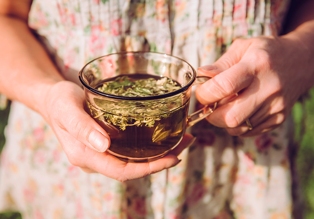 Frau hält eine Tasse mit Kräutertee in der Hand. 