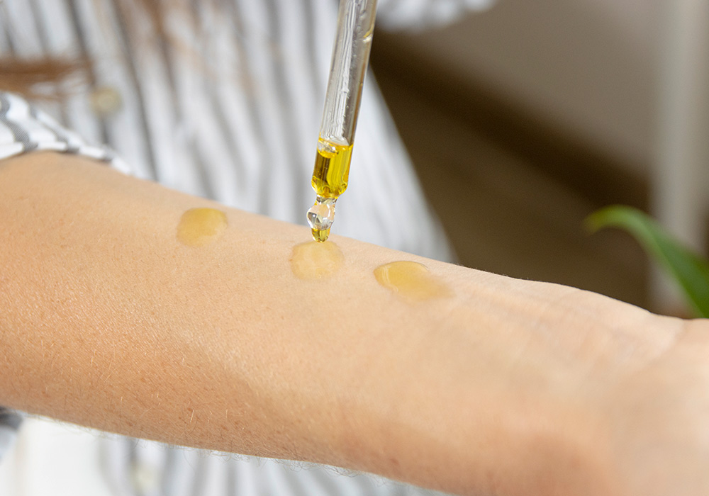 Haut eines Unterarms, auf dem 3 Tropfen Öl aus einer Pipette zu sehen sind. 