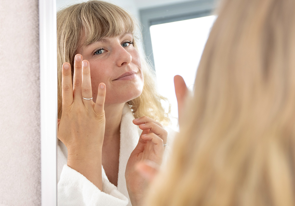 Julia steht vor einem Spiegel und wendet das InnoNature Aloe Hyaluron Serum an