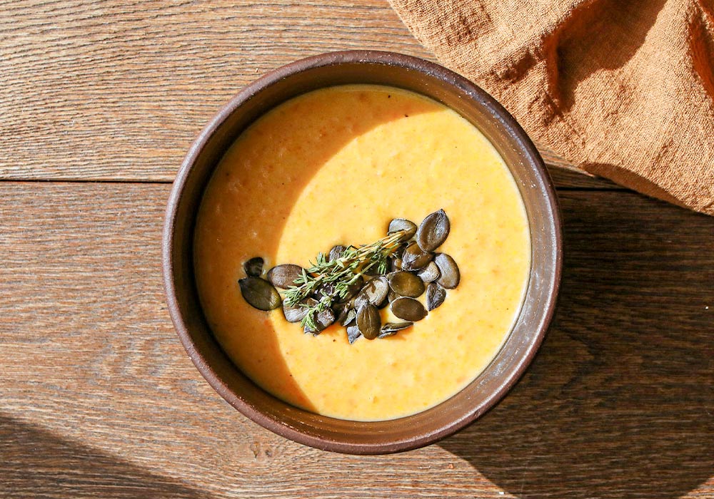 Schale mit orange farbener Suppe mit Kürbiskernen on top.
