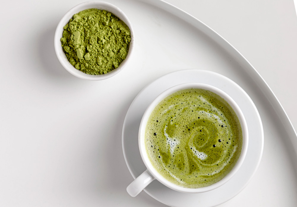 Eine Tasse mit Matcha Tee und eine Schale mit Matcha Pulver auf einem weißen Tablett.