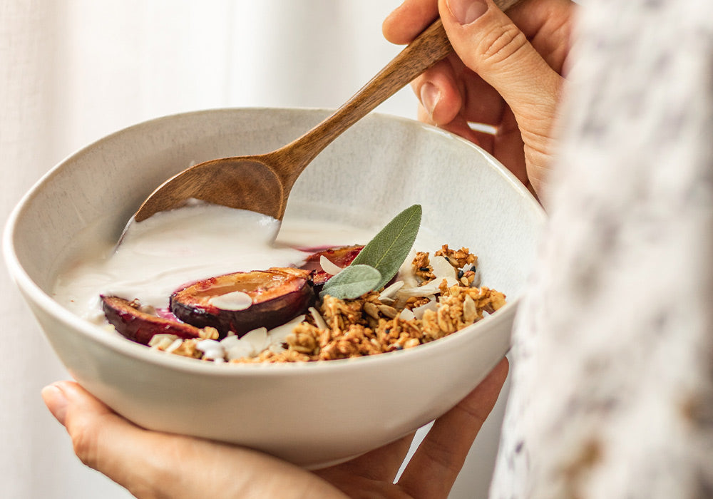 Joghurt Bowl mit Früchten und Granola wird von einer Frau gehalten