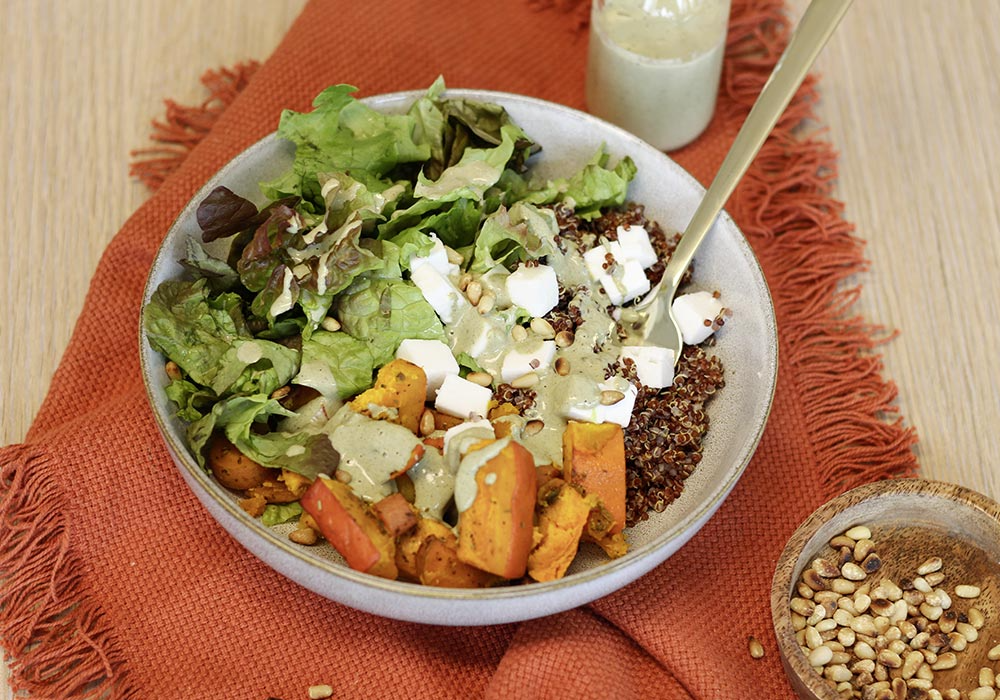 Gebackener Kürbis mit veganem Feta, Pinienkerne und Kürbiskernmus-Dressing. Außerdem ist eine kleine Holzschüssel mit Pinienkernen und ein rotes Tuch zu sehen.