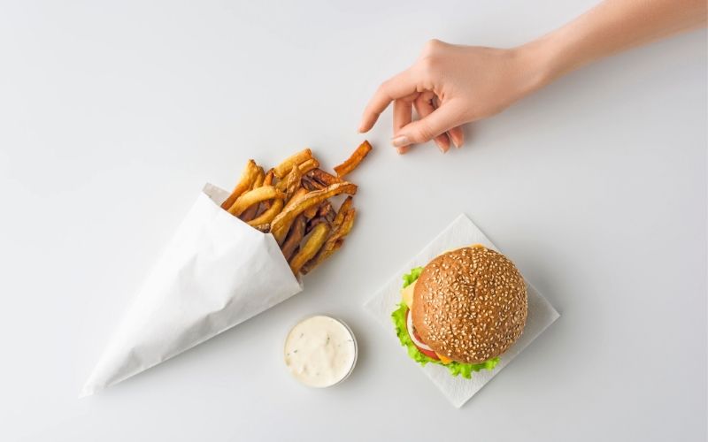 Eine Tüte Pommes und ein Burger mit Majo auf einem weißen Tisch