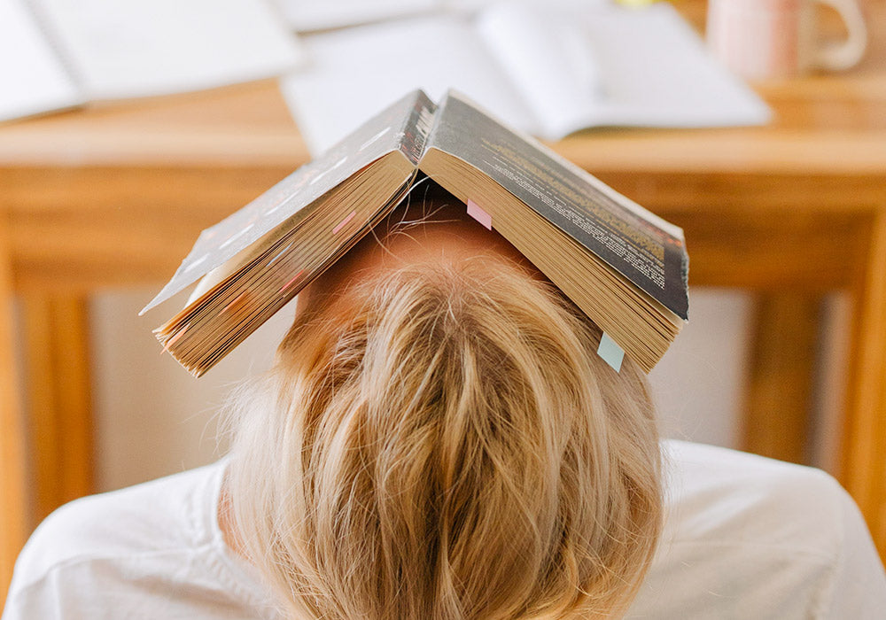 Frau lehnt sich zurück mit aufgeschlagenem Buch über dem Gesicht.