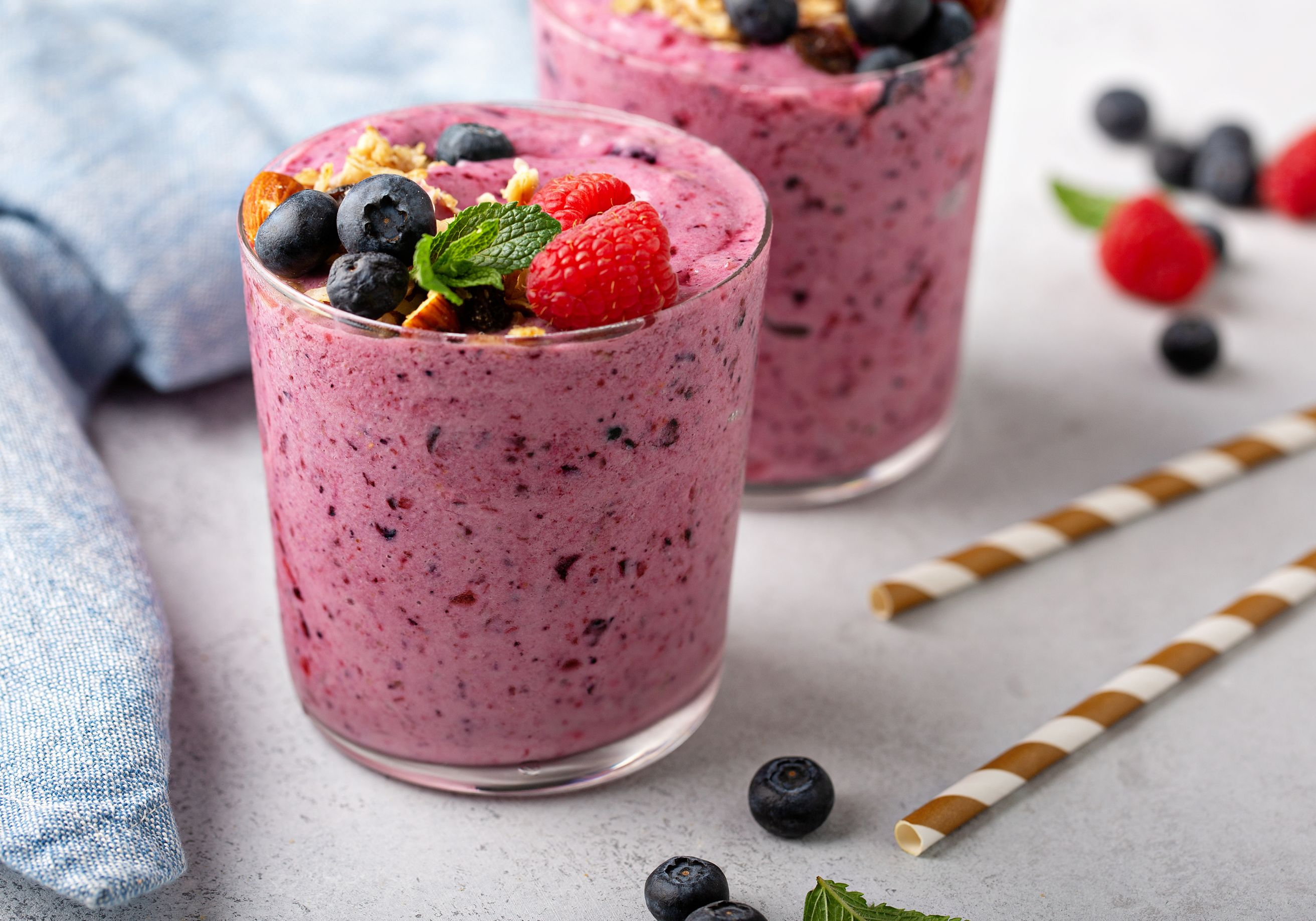Zwei Gläser mit einem roten Smoothie und Beeren-Topping auf einer grauen Tischplatte.