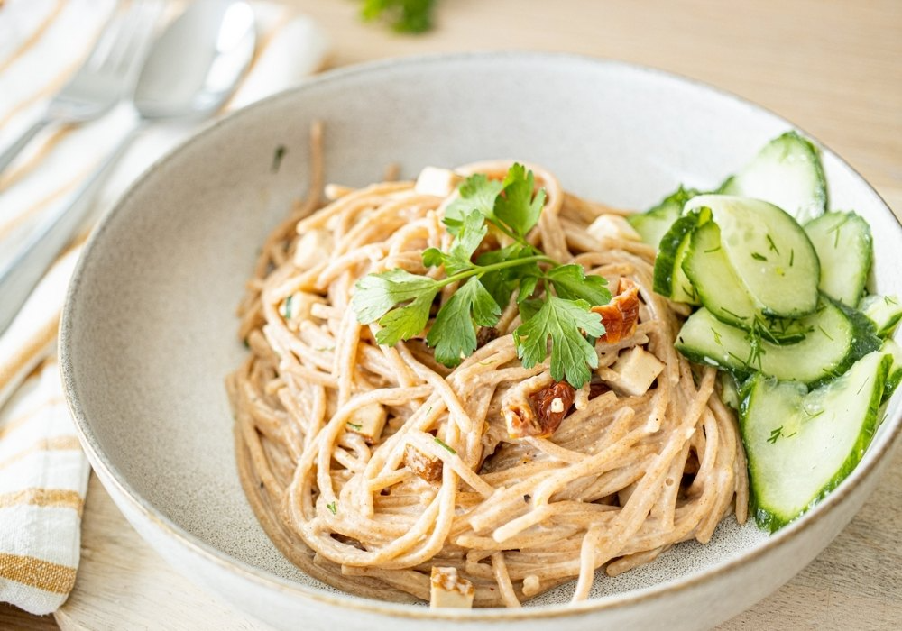 Ein Teller mit veganer Spaghetti Carbonara und Gurkensalat.